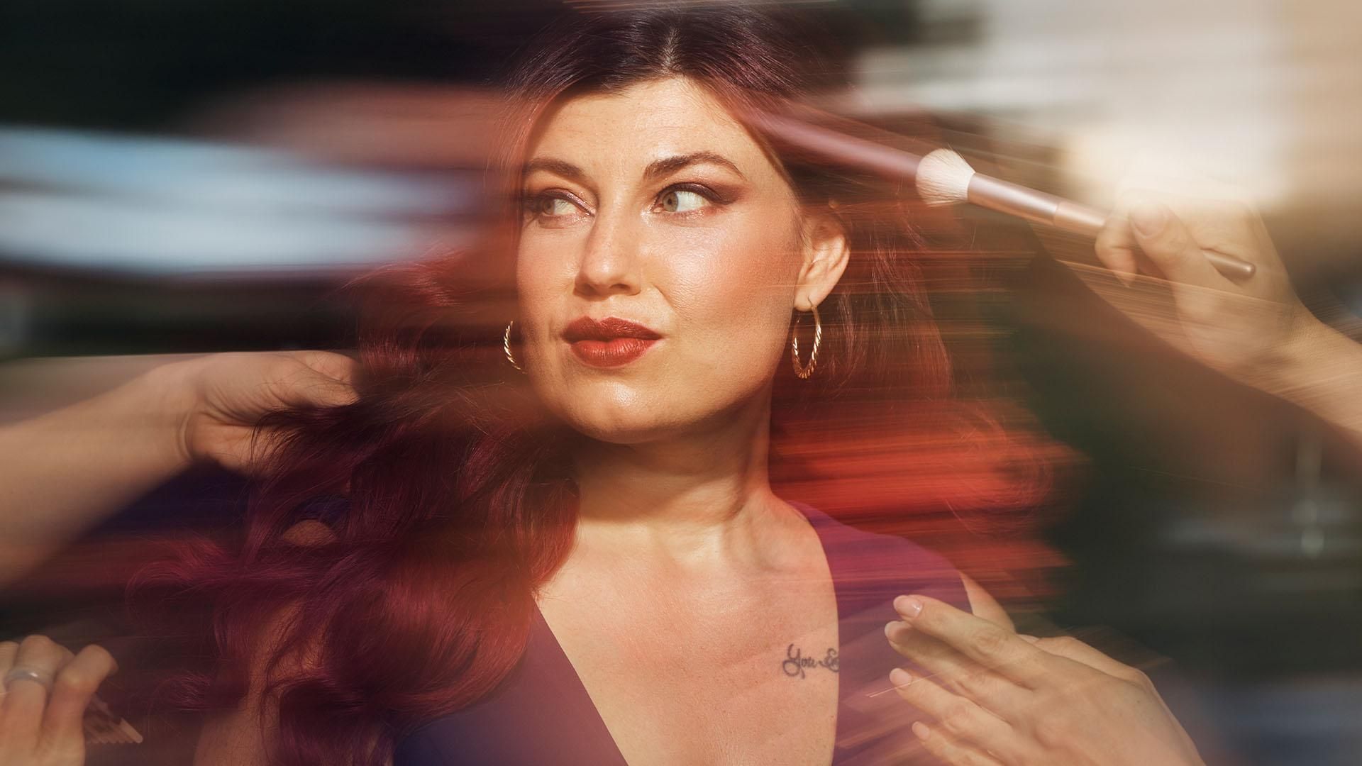 A glamourous woman wearing a purple dress is having her hair and makeup finished, she is looking to the side at somone as they fix her hair. Overlay text reads: "Model and role model."​